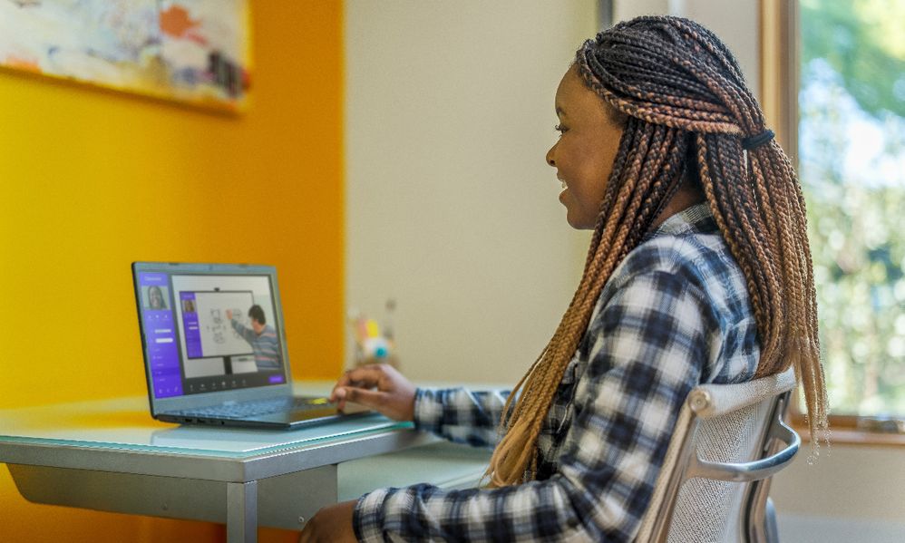 Student with long braids in plaid shirt learning on laptop